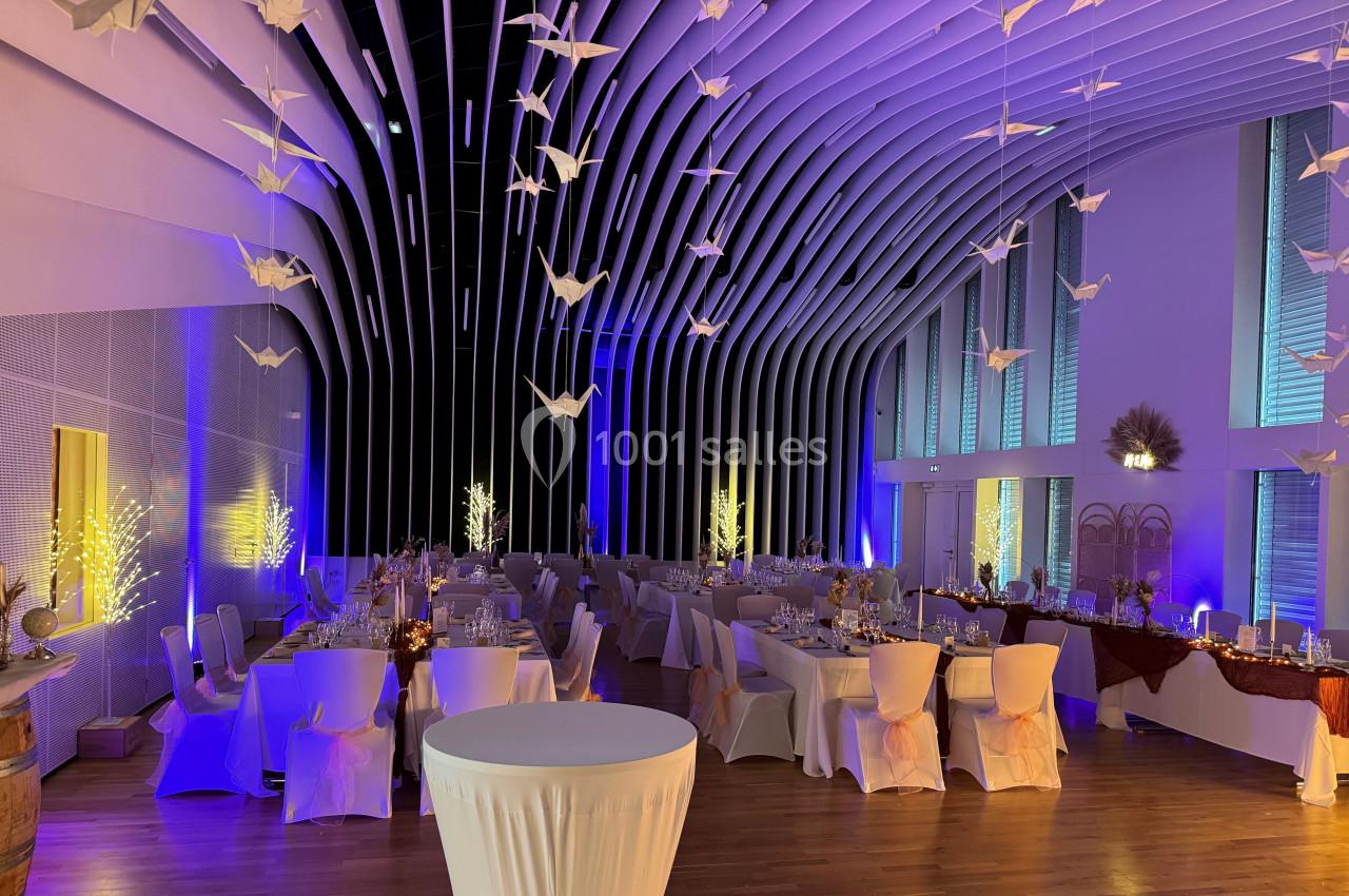 Salle de réception décorée avec des tables dressées, des guirlandes lumineuses et des origamis suspendus au plafond.