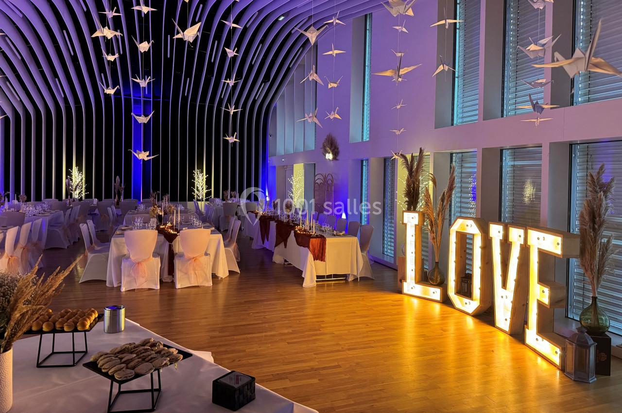 Salle de réception décorée avec des tables dressées, des guirlandes lumineuses et des lettres lumineuses formant ’LOVE’.