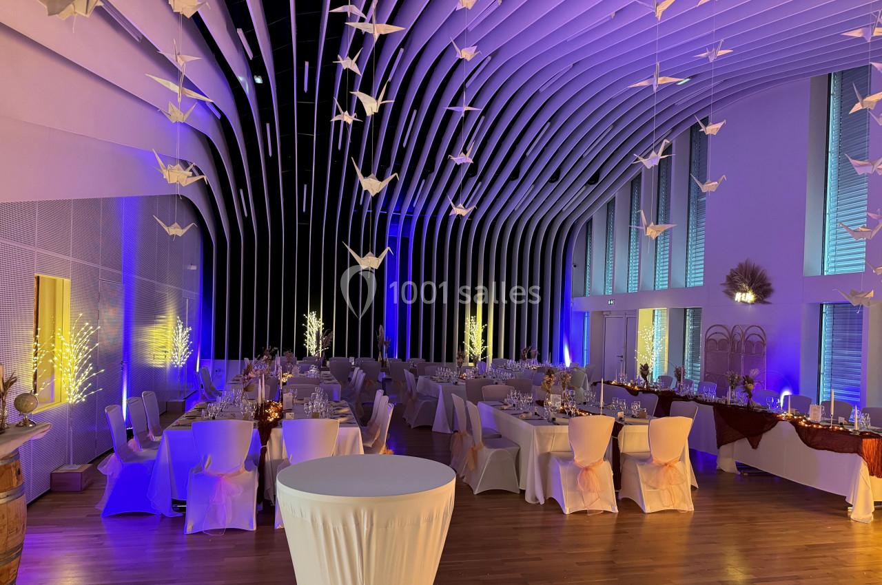 Salle de réception décorée avec des tables dressées, des guirlandes lumineuses et des origamis suspendus au plafond.