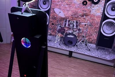 Borne photo avec anneau lumineux devant un décor de scène musicale avec batterie et enceintes.