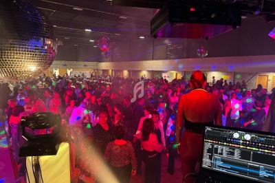 Salle de fête bondée avec des personnes dansant sous des lumières colorées et une boule à facettes.