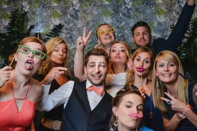 Un groupe de personnes souriantes posant avec des accessoires ludiques devant un fond de feuillage.