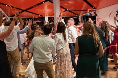 Groupe de personnes dansant sous un plafond rouge, tenant des rubans colorés dans une ambiance festive.