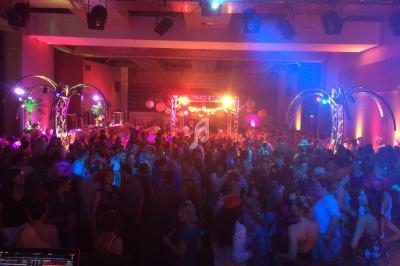 Salle comble avec des personnes dansant sous des éclairages colorés, entourées de décorations festives et de structures…