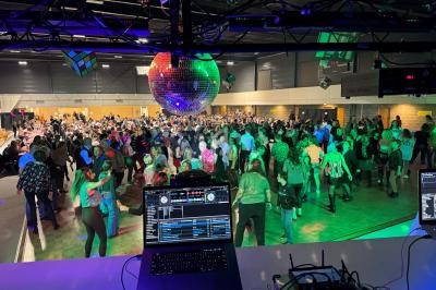 Salle comble avec des personnes dansant sous une boule à facettes, vue depuis une table de mixage.