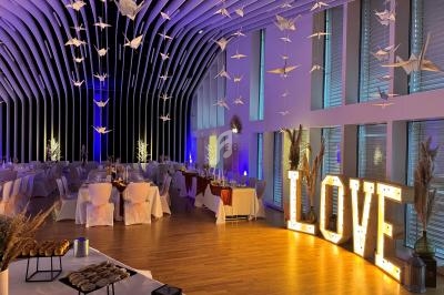 Salle de réception décorée avec des tables dressées, des guirlandes lumineuses et des origamis suspendus.