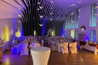 Salle de réception élégamment décorée avec des tables dressées, éclairage violet et origamis suspendus au plafond.