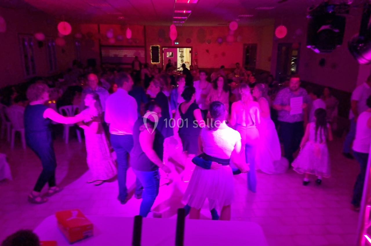 Groupe de personnes dansant dans une salle éclairée par des lumières roses pendant une fête ou un événement.