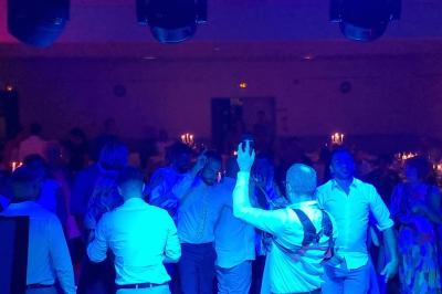 Vue depuis une scène sur une salle de réception où des invités dansent sous des lumières colorées.