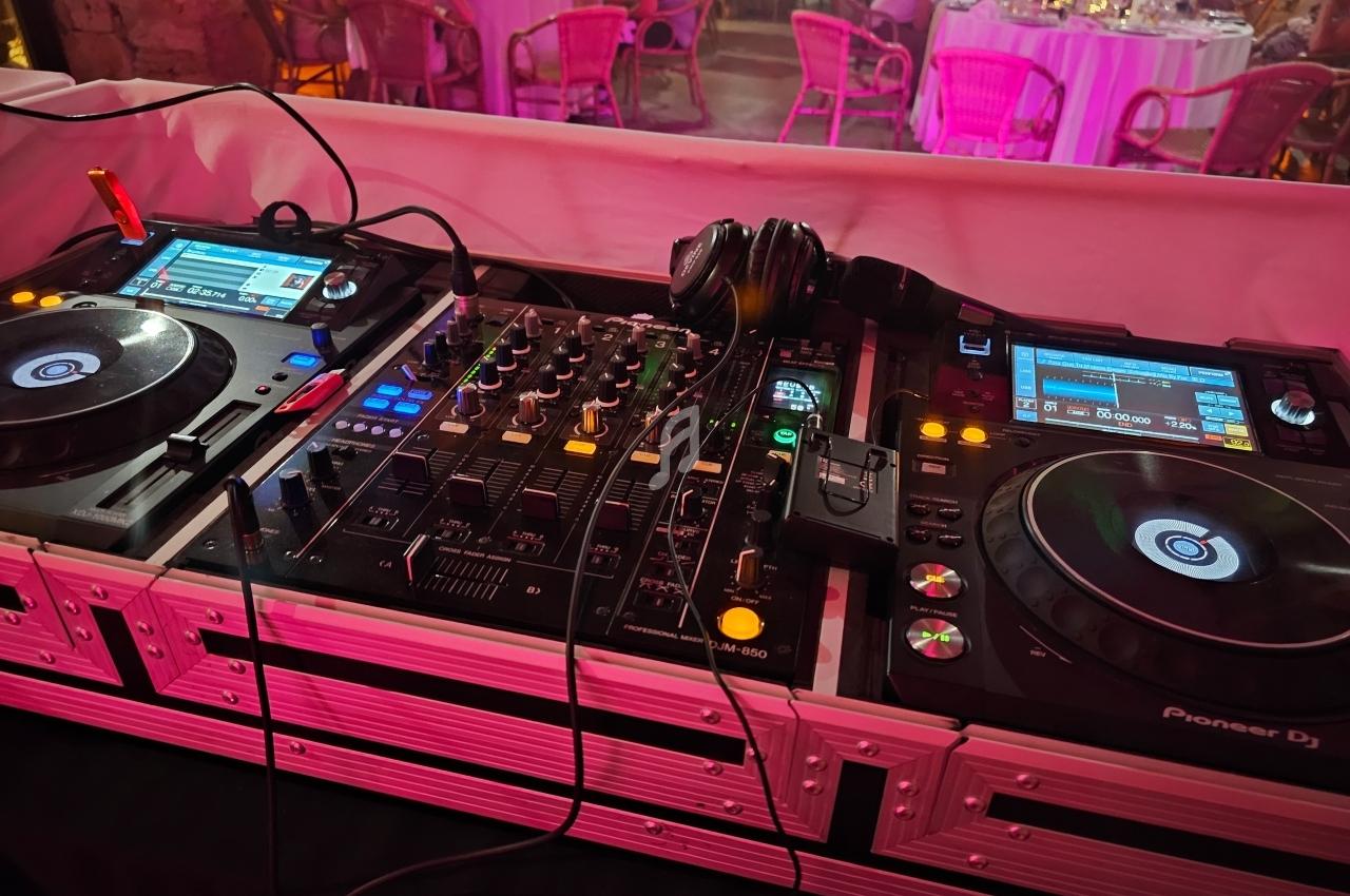 Table de mixage DJ avec platines, casque audio et éclairage rose, en arrière-plan des tables de dîner.
