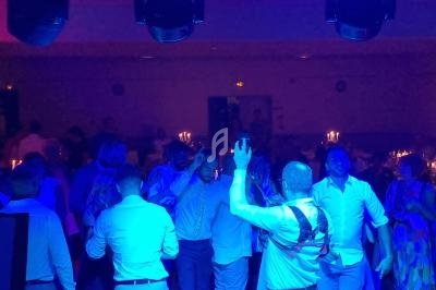 Des personnes dansent sous des lumières bleues dans une salle sombre, avec des bougies visibles en arrière-plan.