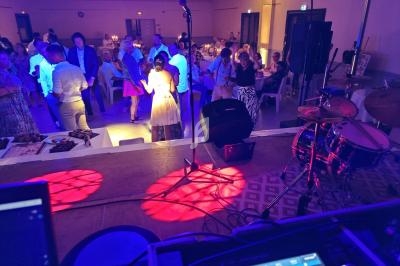 Vue depuis une scène sur une salle de réception avec des invités dansant sous des lumières colorées.