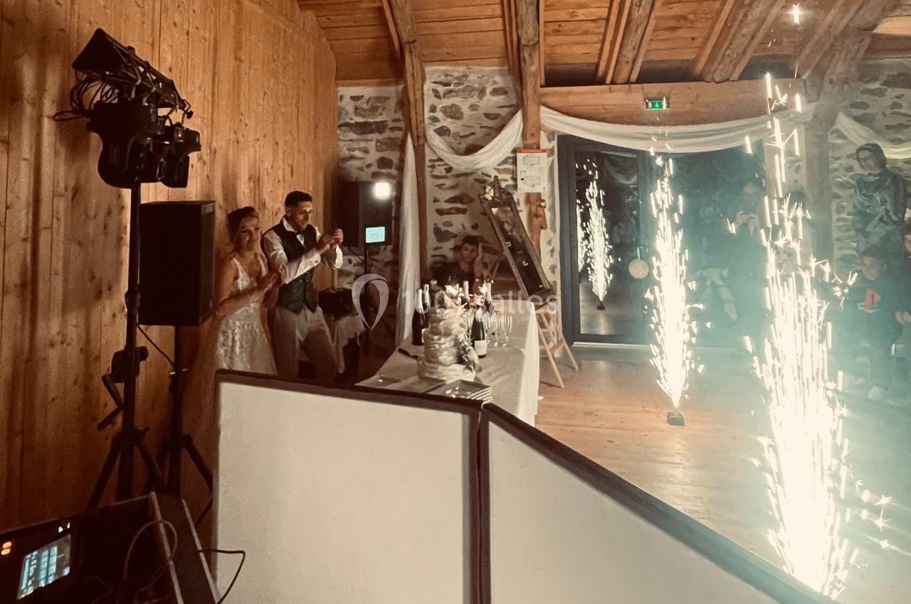 Un couple de mariés trinque près d'une table décorée, avec des étincelles illuminant une salle en bois.