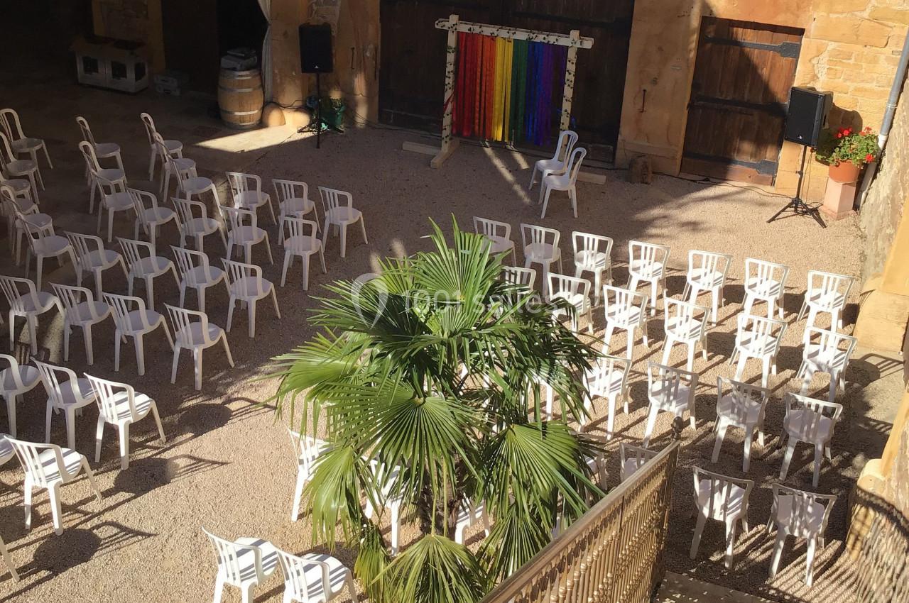 Chaises blanches disposées en rangées dans une cour extérieure ensoleillée avec une scène colorée en arrière-plan.