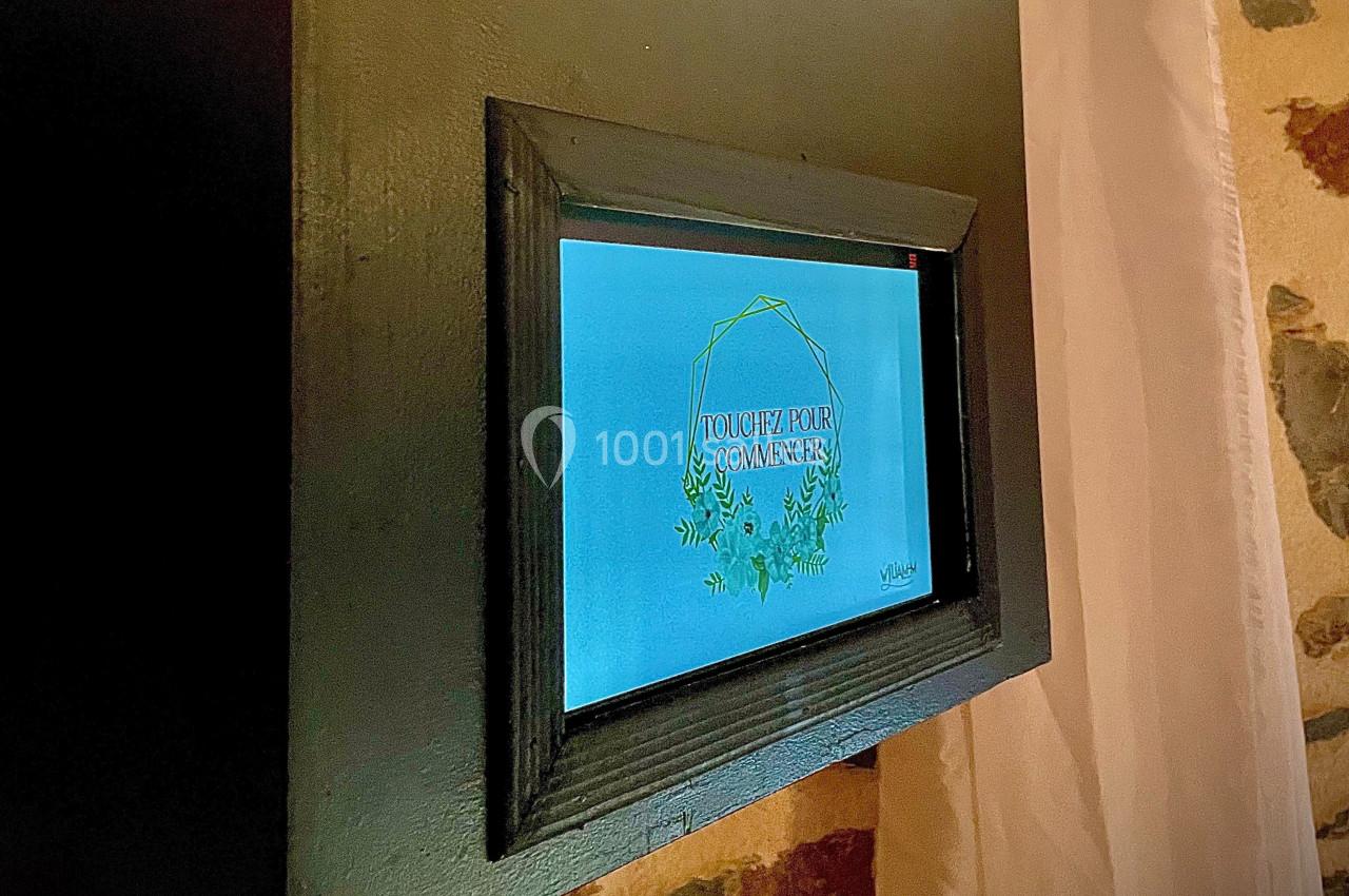 Écran tactile encastré dans un mur affichant le message ’Touchez pour commencer’ entouré d'un motif végétal.