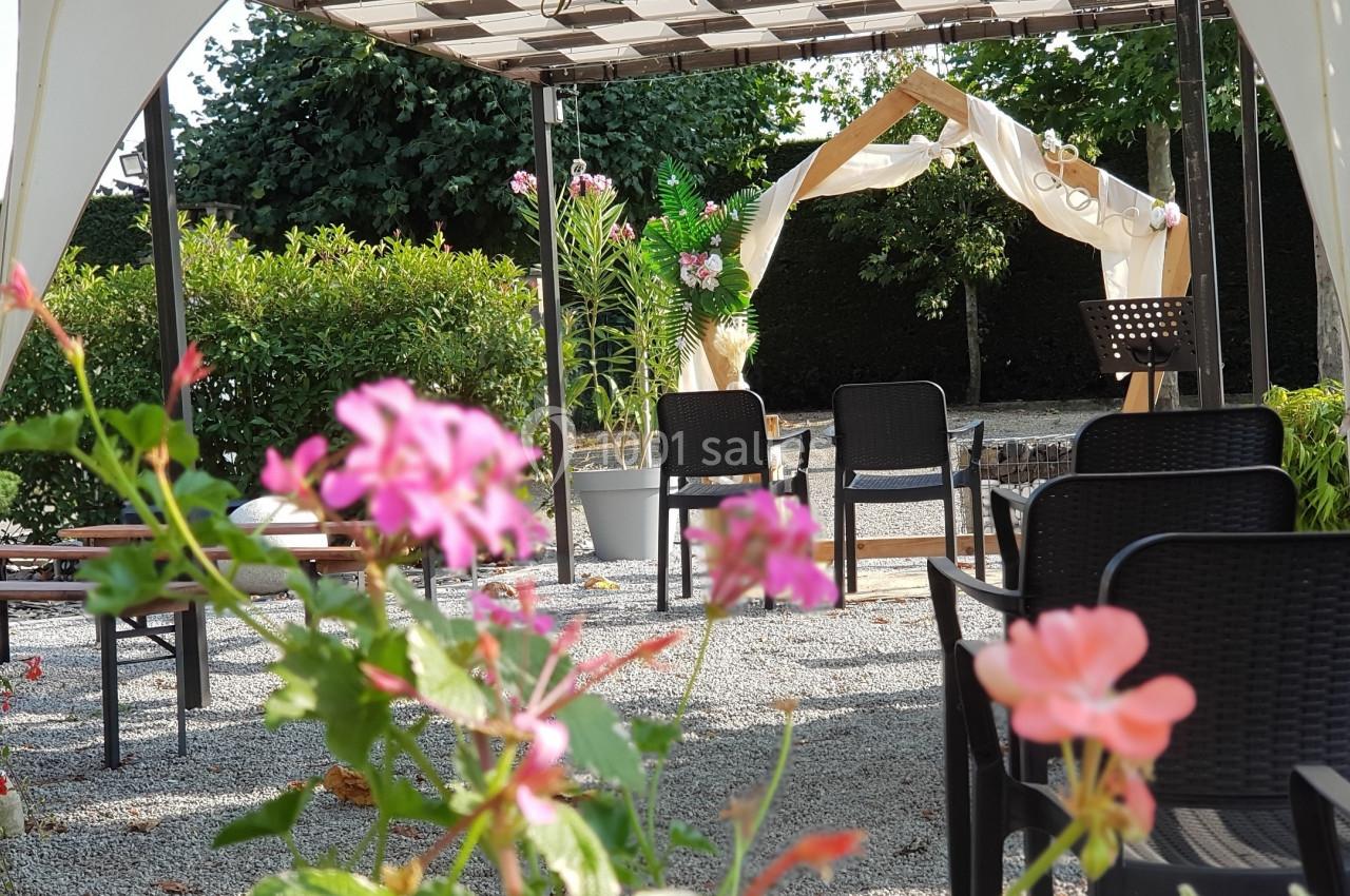 Chaises disposées sous une pergola en extérieur, avec des fleurs au premier plan et une arche décorée en arrière-plan.