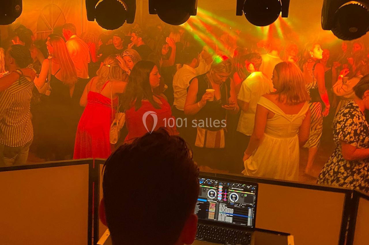 Personnes dansant et discutant dans une ambiance festive avec éclairages colorés, vue depuis la cabine du DJ.