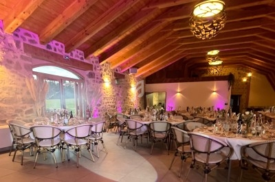 Salle de réception en pierre avec plafond en bois, tables rondes dressées et éclairage chaleureux.