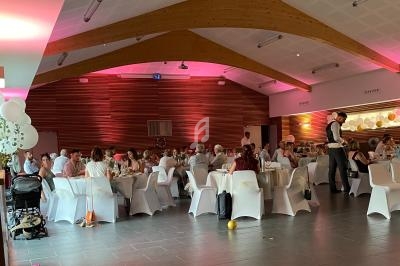 Salle décorée avec des invités assis à des tables rondes lors d'un événement festif, éclairage rose au plafond.