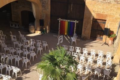 Cour intérieure en pierre avec des chaises blanches disposées face à une scène ornée de rideaux colorés.