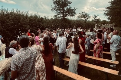 Groupe de personnes rassemblées en extérieur lors d'un événement festif, entourées de bancs en bois et de végétation.