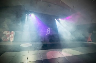 Salle de fête avec piste de danse éclairée par des projecteurs colorés et décorations en arrière-plan.