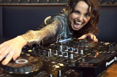 Une femme souriante mixe de la musique sur une table de mixage dans un environnement festif.