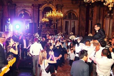 Groupe de personnes dans une salle ornée de lustres, célébrant avec musique et danse lors d'un événement festif.