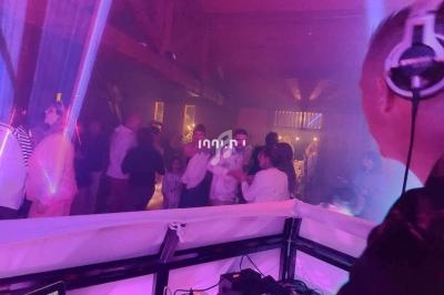 Un DJ mixe sur scène dans une ambiance lumineuse violette, avec des personnes dansant en arrière-plan.