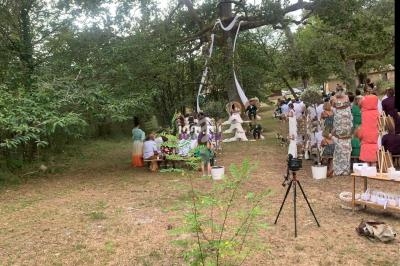 Cérémonie en plein air sous un grand arbre, avec des invités assis et des décorations suspendues aux branches.