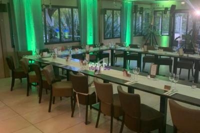 Salle de réception moderne avec tables disposées en U, chaises en bois et éclairage d’ambiance vert.