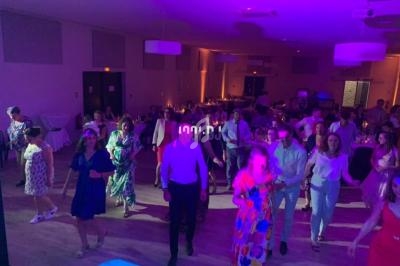 Des personnes dansent en groupe dans une salle éclairée par des lumières colorées, lors d'un événement festif.