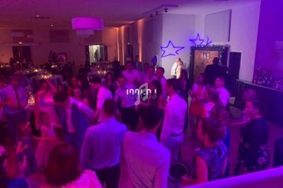 Des invités dansent dans une salle de réception éclairée par des lumières colorées lors d'une fête ou d'un mariage.