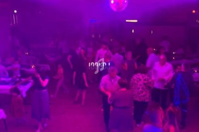 Personnes dansant et discutant sous des lumières colorées dans une salle de fête avec une boule disco au plafond.