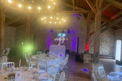 Salle de réception rustique avec murs en pierre, tables dressées et éclairages colorés.