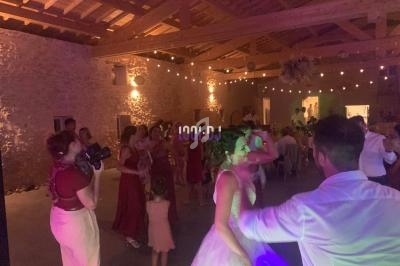 Des invités dansent dans une salle en pierre éclairée par des guirlandes lumineuses lors d'une fête ou d'un mariage.