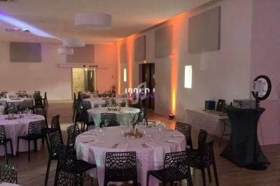 Salle de réception avec tables rondes dressées, chaises noires ajourées et éclairage d'ambiance chaleureux.