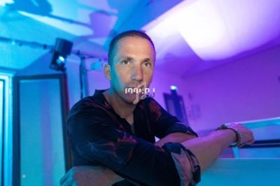 Homme appuyé sur une surface dans une pièce éclairée par des lumières bleues et violettes.