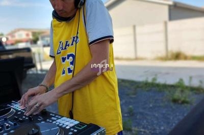 Un DJ mixant en extérieur, portant un maillot jaune et un casque audio, avec des maisons en arrière-plan.