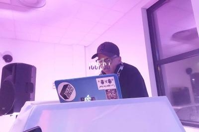 Un DJ mixe de la musique sur un ordinateur portable dans une salle éclairée par une lumière rose.