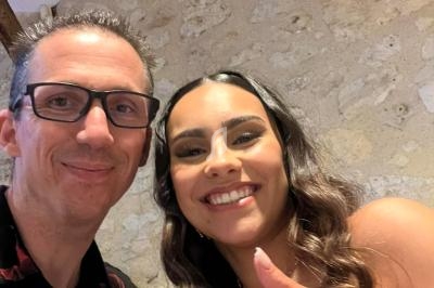 Deux personnes souriantes posent pour une photo devant un mur en pierre, levant le pouce en signe d'approbation.