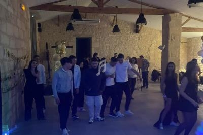 Des personnes dansent en groupe dans une salle en pierre éclairée, avec des décorations et un espace DJ visible au premier…