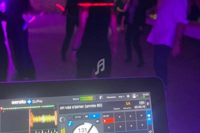 Personnes dansant dans une salle faiblement éclairée, avec en premier plan un écran de mixage de DJ affichant une chanson.