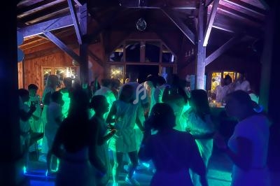 Des personnes dansent sous des lumières colorées dans une salle en bois, lors d'un événement festif en soirée.