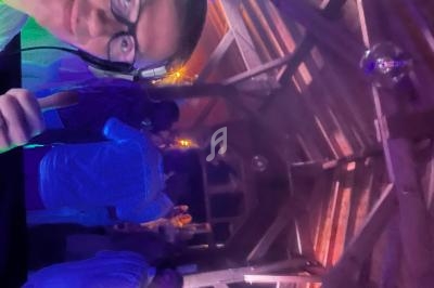 Une personne avec un casque audio dans une salle en bois éclairée par des lumières colorées, avec des gens en arrière-plan.