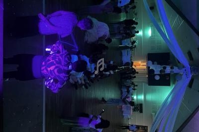 Personnes dansant et discutant dans une salle de réception décorée, éclairée par des lumières tamisées et colorées.