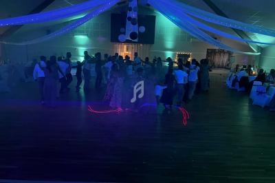 Groupe de personnes dansant en cercle dans une salle de réception décorée avec des lumières colorées et des guirlandes…