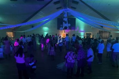 Salle de réception éclairée par des lumières colorées, avec des invités rassemblés et dansant lors d'un événement festif.