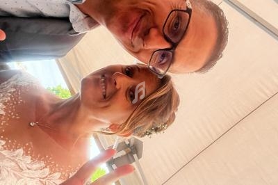 Un couple souriant prend un selfie sous une structure en toile, la femme fait un signe de paix avec ses doigts.