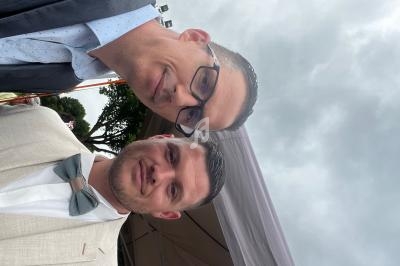 Deux hommes en costume posant ensemble sous un ciel nuageux, avec une tente visible en arrière-plan.